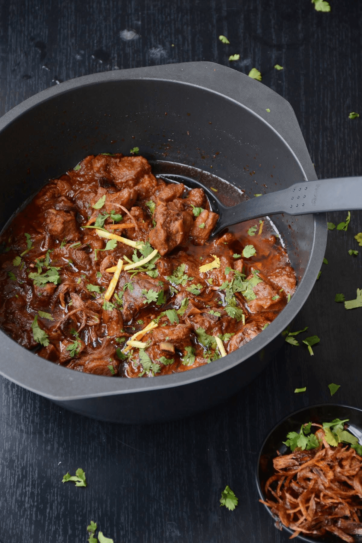 A deep red slow-cooked curry garnished with coriander and ginger